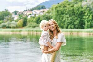 Outdoor portrait of happy young mother with adorable preschooler son, enjoying nice day next to lake photo