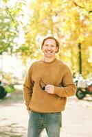 Outdoor autumn portrait of handsome young man wearing brown fuzzy fleece sweater, holding sunglasses in hands photo