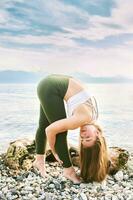 Outdoor portrait of young beautiful woman practicing yoga by the lake photo