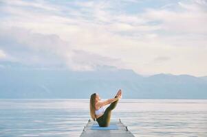Outdoor portrait of young beautiful woman practicing yoga by the lake photo