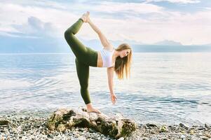 al aire libre retrato de joven hermosa mujer practicando yoga por el lago foto