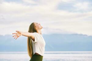 Outdoor portrait of beautiful young woman enjoying nice sunny day by the mountain lake, arms wide open, breathing fresh alpine air photo