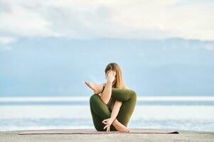 Outdoor portrait of young beautiful woman practicing yoga by the lake photo