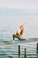 al aire libre retrato de joven hermosa mujer practicando yoga por el lago foto