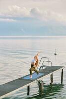 Outdoor portrait of young beautiful woman practicing yoga by the lake photo