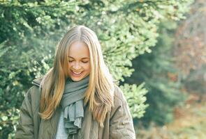 Outdoor portrait of beautiful blond woman, lokking down, wearing warm scarf and winter jacket, walking in pine forest photo