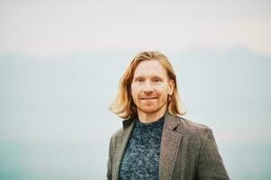 Outdoor portrait of young red haired man, wearing pullover and coat, cold foggy day photo