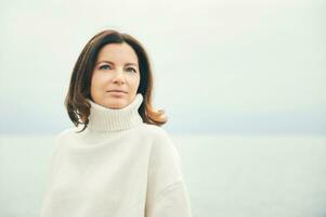 Outdoor portraiit of beautiful woman wearing white pullover, relaxing next to lake or sea photo