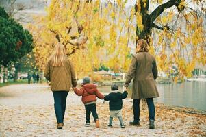 al aire libre retrato de joven contento familia de cuatro, madre y padre jugando con niños en otoño parque por el lago, frío clima foto