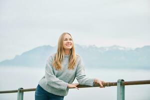 Outdoor portrait of happy beautiful young woman relaxing in mountains over the clouds, wearing grey pullover photo