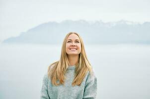 Outdoor portrait of happy beautiful young woman relaxing in mountains over the clouds, wearing grey pullover photo