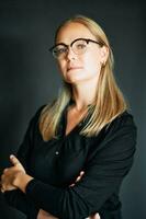 Portrait of beautiful young woman with blond hair, wearing glasses, posing on dark background photo