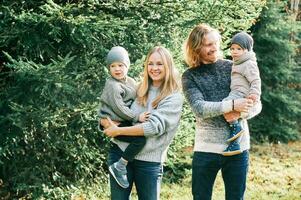 al aire libre retrato de hermosa contento joven familia de 4 4 posando en pino bosque, vistiendo calentar jerseys, Pareja con niñito chico y bebé niña teniendo bueno hora a naturaleza, frío clima foto