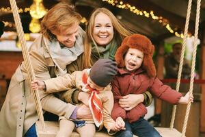 Outdoor portrait of happy young family at Christmas market, parents with 2 little children enjoying holidays, travel with kids photo