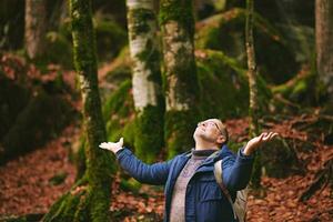 Handsome middle age man hiking in forest, wearing warm jacket, backpack and glasses photo
