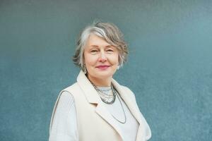 Outdoor portrait of beautiful 55 - 60 year old woman posing next to blue background wall photo