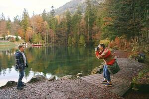 Young happy woman taking picture of preteen kid by mountain lake, family travel with children photo