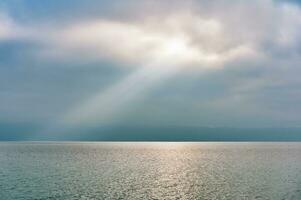 Rays of light falling through clouds on calm water surface photo