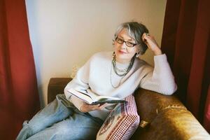Interior portrait of 50 - 55 year old woman sitting on couch , wearing glasses photo