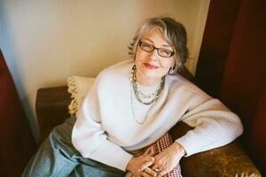 Interior portrait of 50 - 55 year old woman sitting on couch , wearing glasses photo