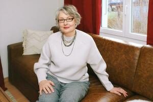 Interior portrait of 50 - 55 year old woman sitting on couch , wearing glasses photo