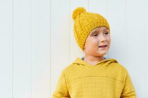 Close up portrait of adorable 5 year old kid wearing yellow sweatshirt and hat, posing on white background photo