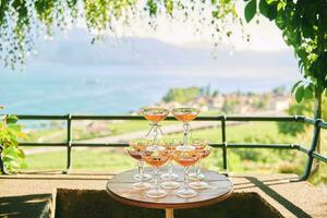 Pyramid of fruit cocktails in vintage glasses standing on a table in a cozy summer garden with lake view photo