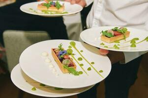 Close up image of waiter carries several plates of colored vegetable tartlets photo