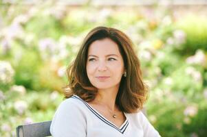 Outdoor portrait of beautiful 40 - 45 years old woman sitting on bench ib green park, healthy lifestyle photo