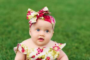 Outdoor portrait of adorable 6 months old baby girl playing in summer park, child crawling on fresh green lawn photo