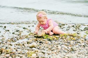 Outdoor portrait of adorable baby girl playing with seaweed by the river, wearing pink swimsuit photo