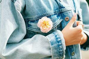 Moda detalles, mujer vistiendo ligero mezclilla chaqueta con Fresco floreciente Rosa en bolsillo foto