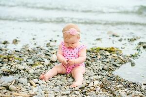 Outdoor portrait of adorable baby girl playing with seaweed by the river, wearing pink swimsuit photo