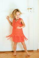 Portrait of happy little girl dancing at home wearing bright orange dress photo
