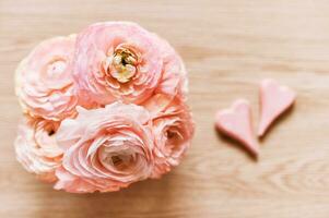 Beautiful bouquet of pink ranunculus with 2 hearts, top view, wooden background photo