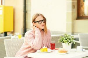 Outdoor portrait of cute young teen girl resting in cafe, listening music or podcast photo