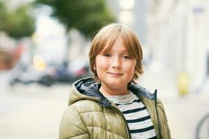 Outdoor portrait of handsome 10 year old kid boy, wearing warm jacket, looking straight at camera, posing on city street photo