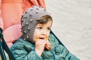 Toddler sitting in stroller and eating croissant, pastry snack photo