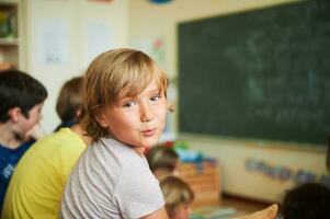 linda pequeño chico trabajando en aula, educación, espalda a colegio concepto foto