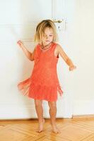 Portrait of happy little girl dancing at home wearing bright orange dress photo