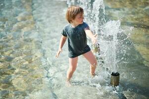 Outdoor portrait of happy little boy playing inside of city fountain on a hot summer day photo