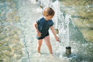 Outdoor portrait of happy little boy playing inside of city fountain on a hot summer day photo