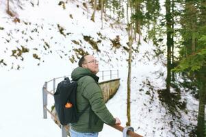 Outdoor portrait of middle age 55 - 60 year old man hiking in winter forest, wearing warm jacket and black backpack photo