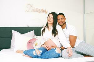 Indoor portrait of happy young family, pregnant woman with her loving husband relaxing on bed photo