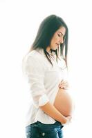 iluminar desde el fondo retrato de joven embarazada mujer, vistiendo blanco camisa y pantalones foto