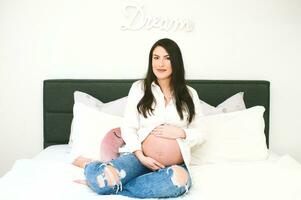 Indoor portrait of beautiful young pregnant woman resting on bed photo