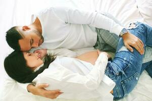 Top view of young pregnant couple cuddling in bed photo