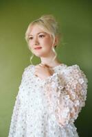 Beauty portrait of pretty young 15 - 16 year old teeenage girl wearing white dress posing on green background photo