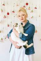 Studio portrait of pretty young teenage 15 - 16 year old girl wearing denim jacket, posing on white background with hanging flowers, holding cute cat, beauty and fashion concept photo