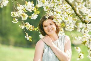 primavera retrato de contento joven mujer en pie debajo floreciente árbol foto